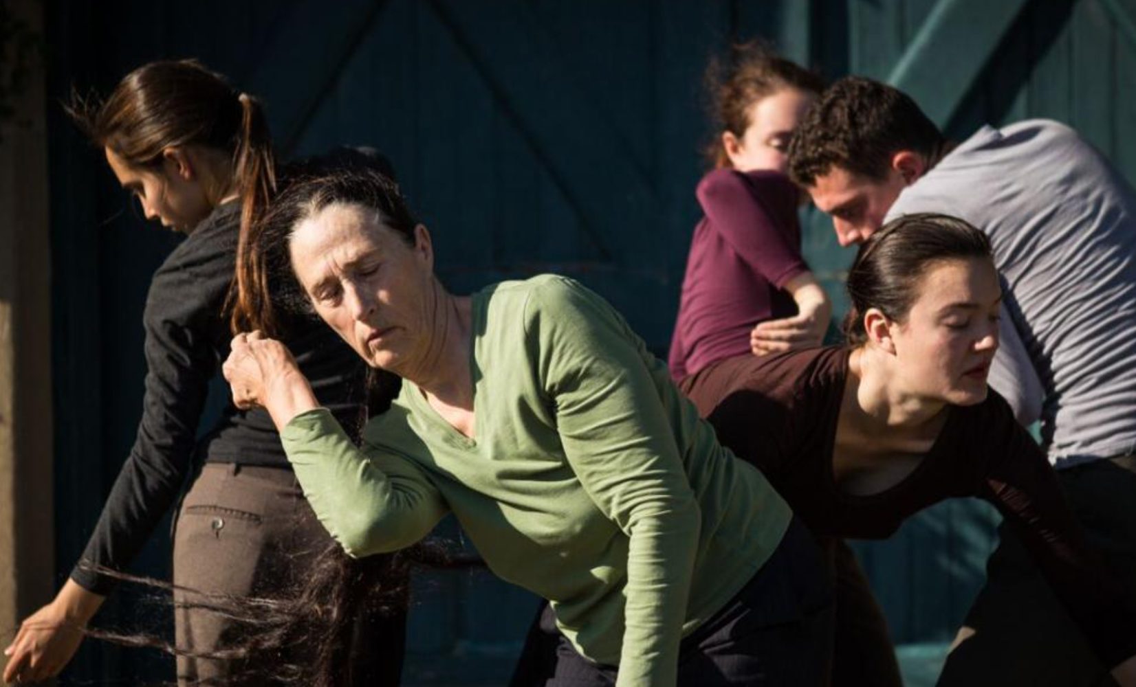 Several dancers entwined facing various directions and reaching around one another. 